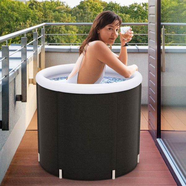 Woman sitting in a portable hot tub on a balcony with trees in the background.
