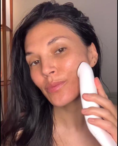 Woman using a white electronic device on her face.