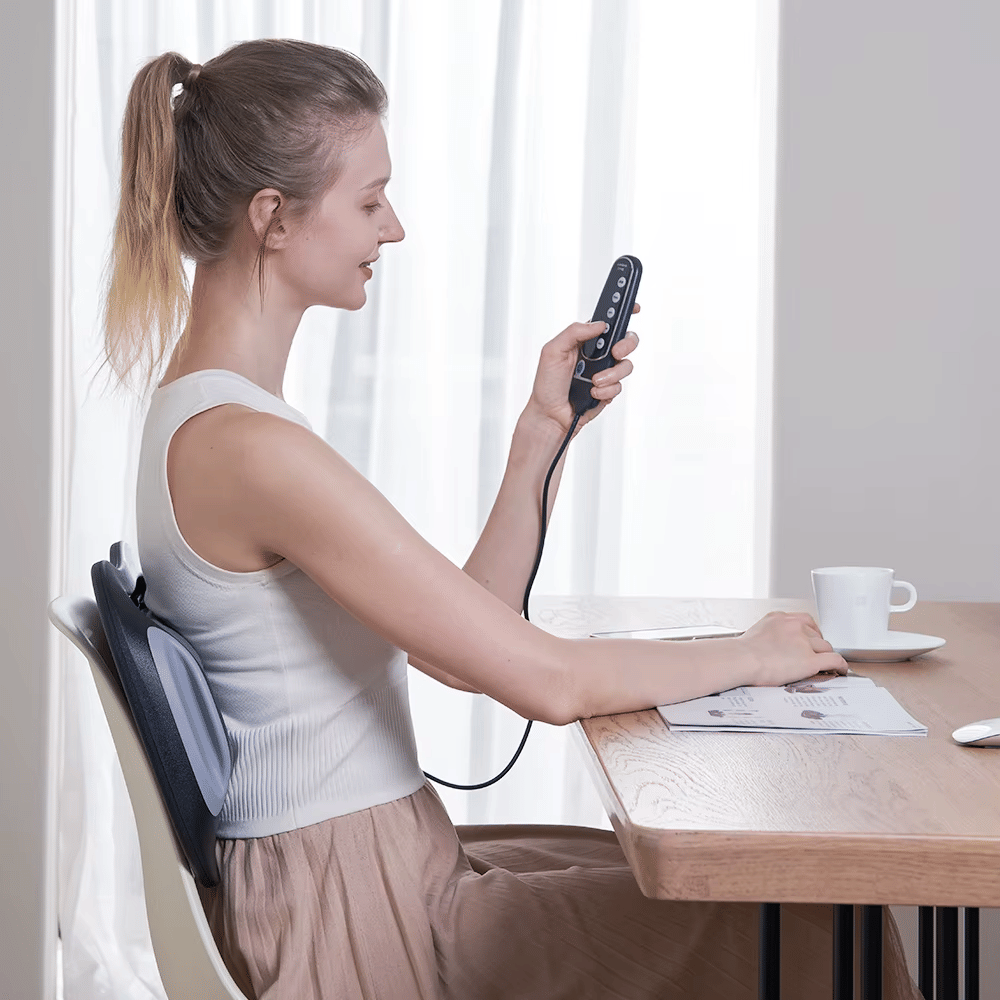 Woman using a back massager at a desk.